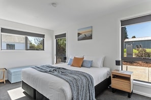 A modern bedroom with a large bed, a bedside table, a window with a view of the outdoors, and a painting on the wall. - Pioneer's Rest - two homes at Branxholm, near Derby (Branxholm)