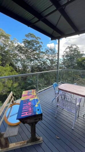 A covered outdoor area with a table and chairs, surrounded by a metal railing, overlooking a forested landscape. - Artists home above rainforest sleeps 10 with pool (Tamborine Mountain)