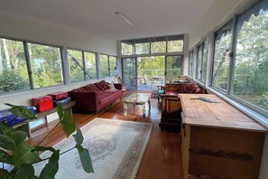 A spacious living area with large windows, a red sofa, a wooden coffee table, and a dining table. - Artists home above rainforest sleeps 10 with pool (Tamborine Mountain)