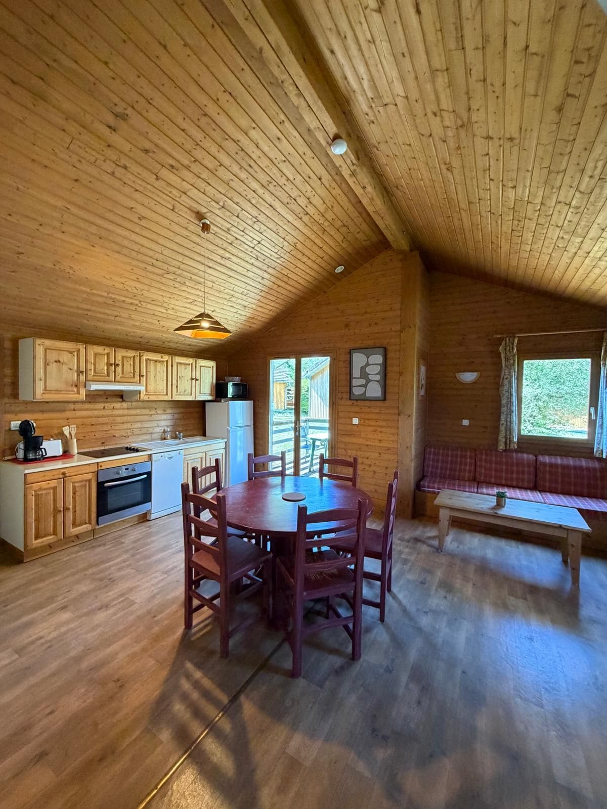 A wooden interior with a dining table, chairs, a kitchen area, and a seating bench.