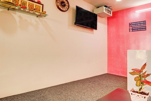 Zona de recepción con televisión, un reloj y un cartel que indica los horarios de registro de entrada y salida.