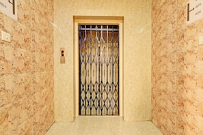 Un ascensor con una puerta metálica, paredes de mármol y un suelo con un diseño similar.