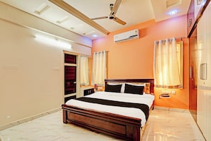 Habitación de hotel con cama, ventilador de techo, aire acondicionado y baño con ducha.