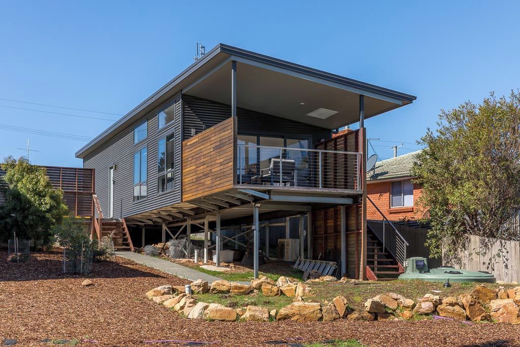 Une maison moderne à deux étages, dotée d’un espace extérieur couvert et d’un mur de soutènement en pierre.