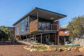 Ein modernes, zweistöckiges Haus mit einer überdachten Terrasse und einer steinernen Stützmauer.
