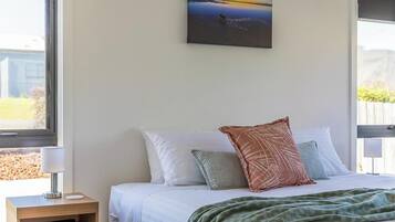 Een slaapkamer met een bed, kussens, een nachtkastje, een lamp en een schilderij aan de muur.