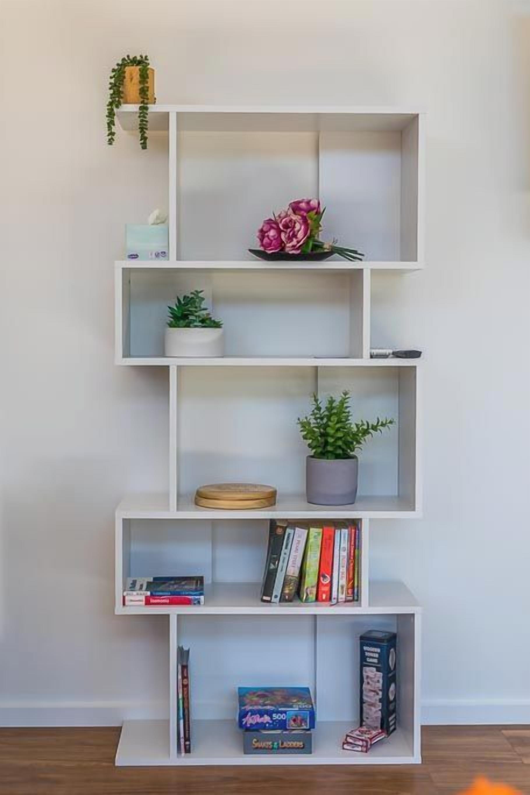 Una estantería blanca con libros, una planta en maceta y un objeto decorativo.