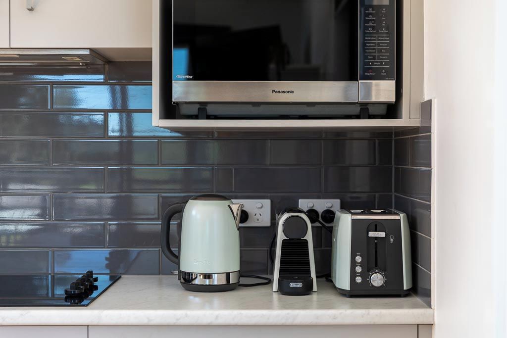 A kitchen with a microwave, a kettle, a toaster, and a coffee maker on the countertop.
