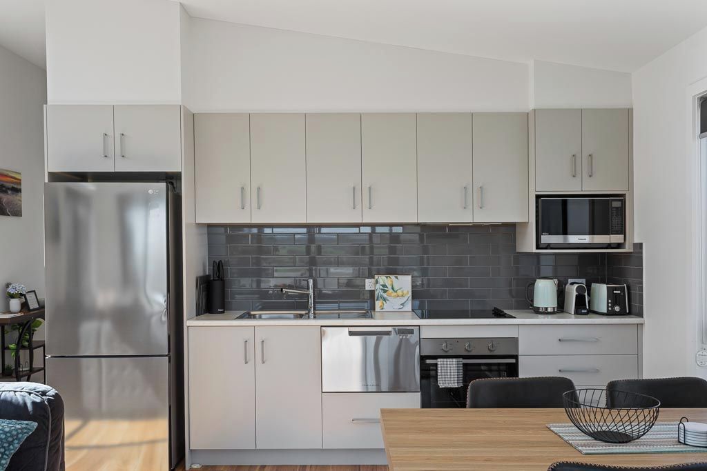Una cocina moderna con electrodomésticos de acero inoxidable, armarios blancos y salpicadero de azulejos.