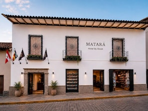Un hotel con fachada blanca, varios balcones con barandillas de hierro forjado y un cartel que dice 'Matará Hotel By Ámak'.