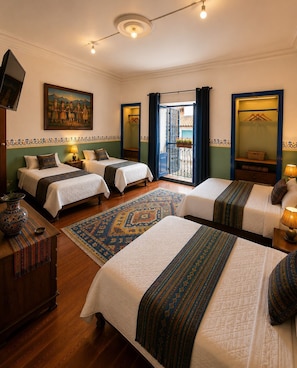 Habitación de hotel con tres camas, un televisor, un cuadro y un balcón con vistas.