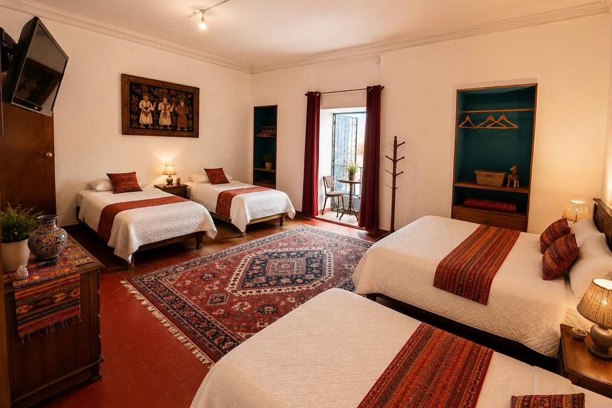 A hotel room with two beds, a large rug, a television, and a painting on the wall.