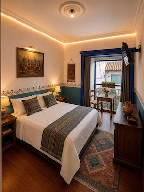A well-lit bedroom with a large bed, a painting, a hanging tapestry, and a view of the outside balcony. - Hotel Colonial Cusco (Wanchag)