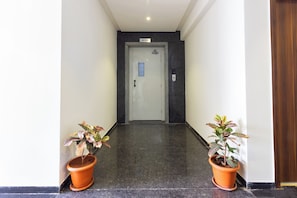 Um corredor com uma porta identificada como '4º Andar', dando acesso a um quarto. Há dois vasos de plantas de cada lado da porta.
