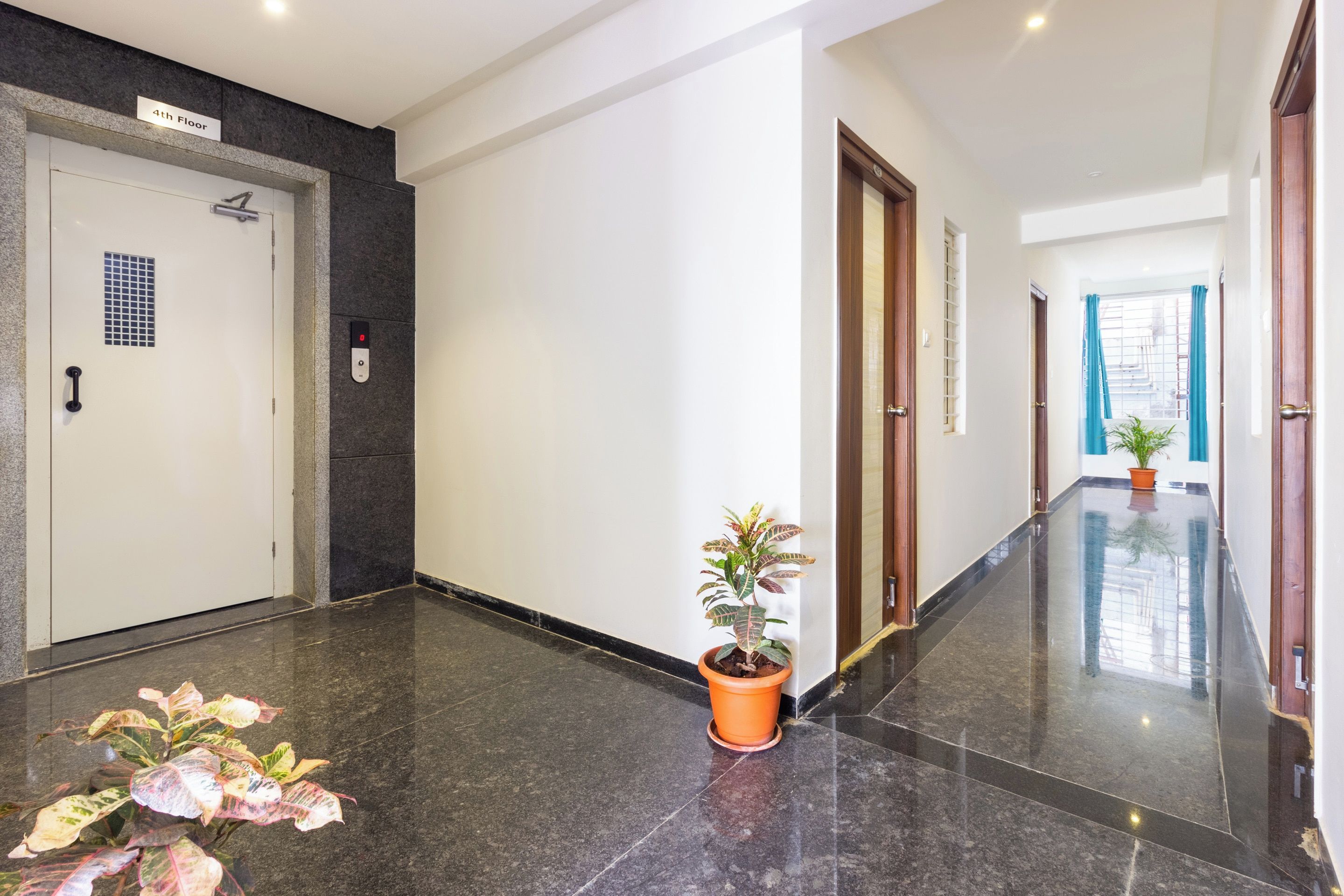 A clean, well-lit hallway with a sign indicating the 4th floor, a door with a security keypad, and a potted plant.