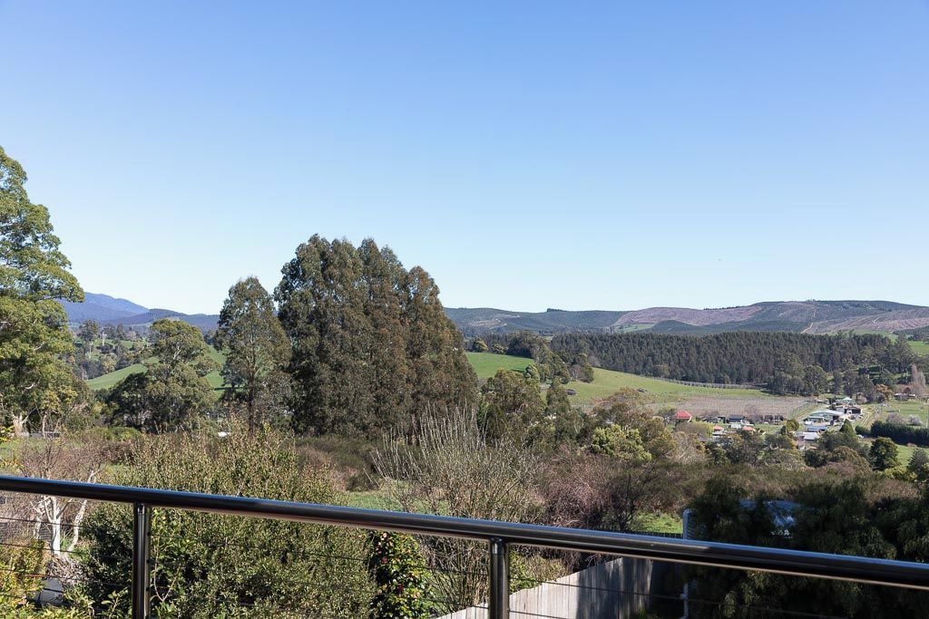 Een prachtig uitzicht vanaf een balkon met een metalen hek, uitkijkend over een glooiend landschap met bomen en een klein dorpje in de verte.