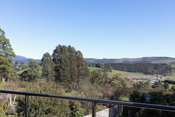 Een prachtig uitzicht vanaf een balkon met een metalen hek, uitkijkend over een glooiend landschap met bomen en een klein dorpje in de verte.