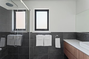 Een moderne badkamer met een douchecabine van glas, een raam en een houten wastafelmeubel met een wastafel.