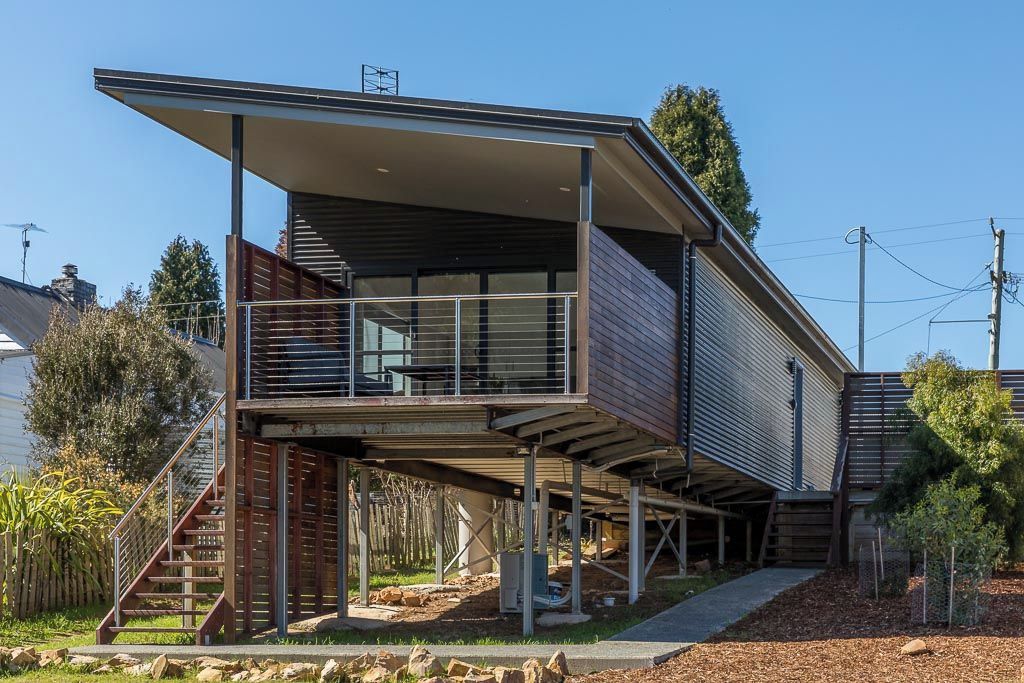 Una casa moderna de dos pisos con techo plano, un balcón y una escalera que lleva al nivel superior.
