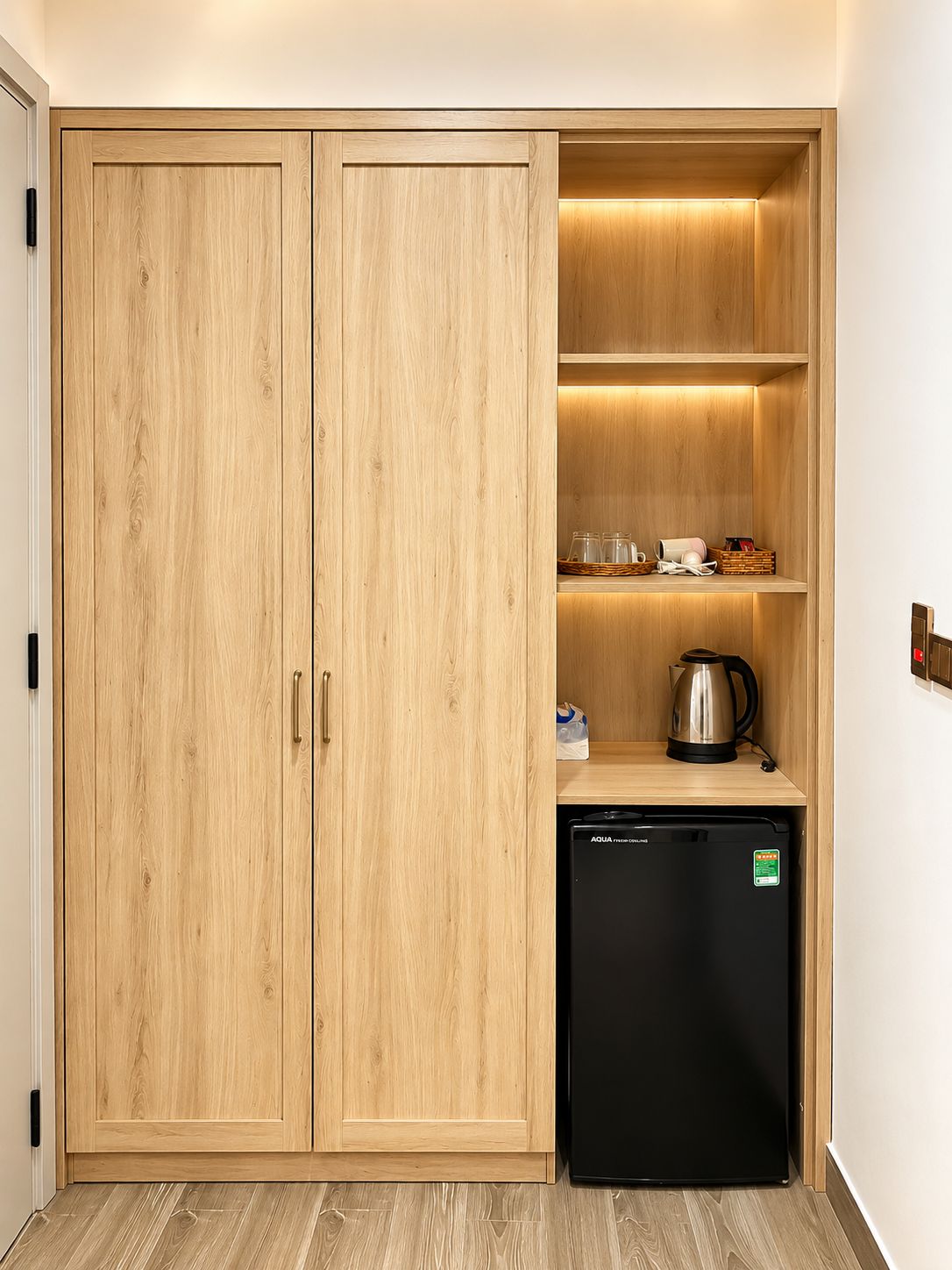 Cocina compacta con muebles de madera, lavavajillas negro y repisas con utensilios de cocina.