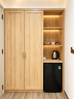A compact kitchen with wooden cabinetry, a black dishwasher, and a shelf with kitchenware. - Sunset Sorento Hotel & Apartment PhuQuoc (Phu Quoc)