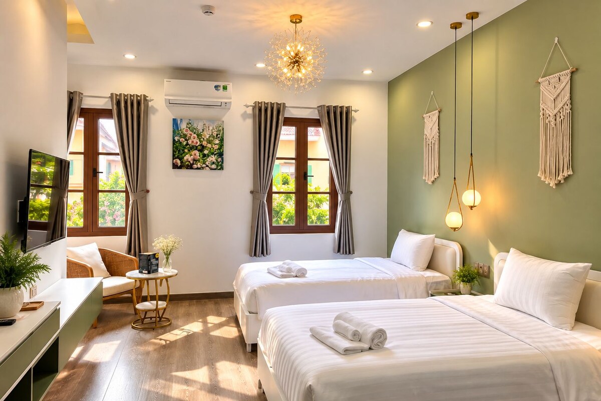 A hotel room with two beds, a desk, a chair, a TV, and a window with curtains.