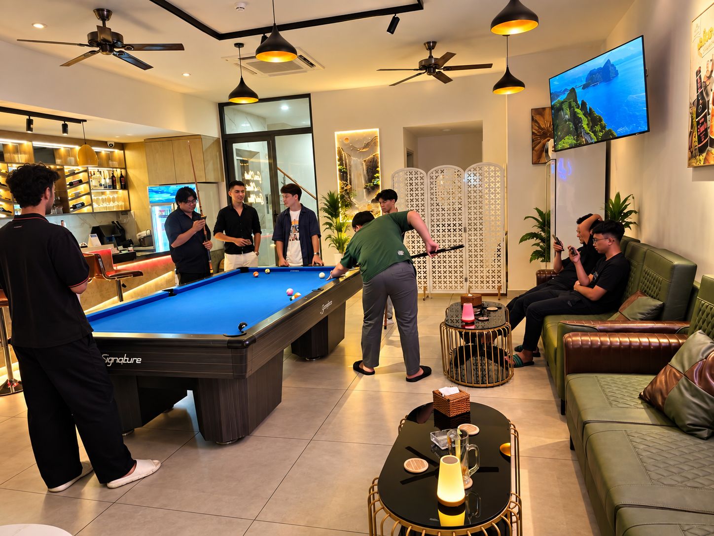 Una mesa de billar en una habitación con ventiladores de techo, televisión y zona de bar.