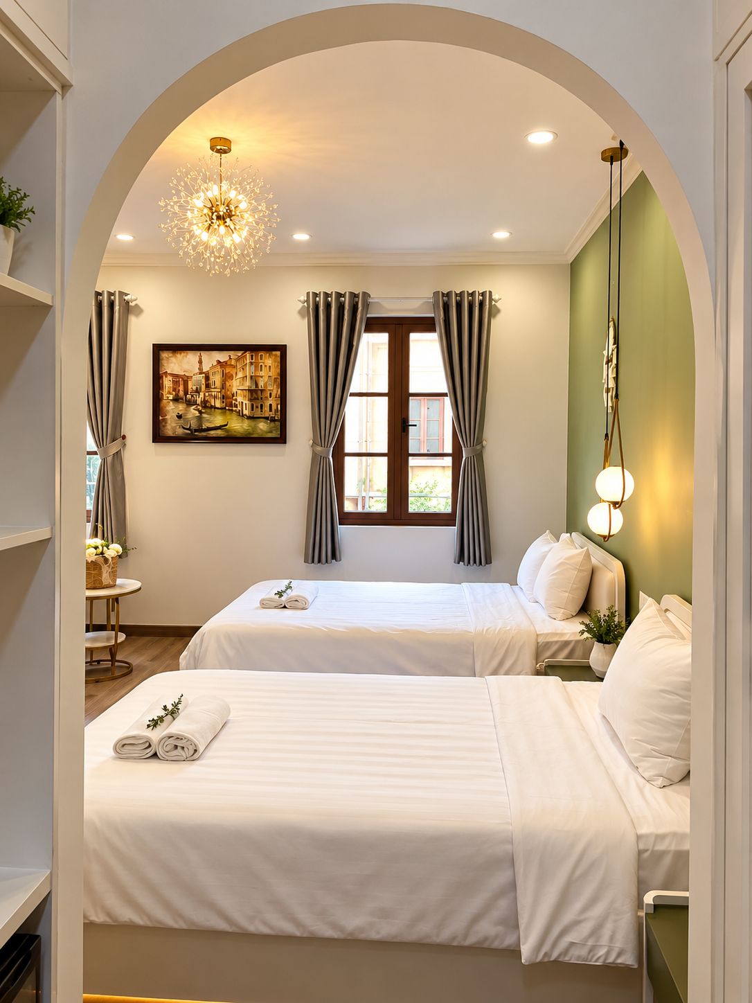 Habitación de hotel con dos camas, un cuadro de un paisaje urbano, una ventana con cortinas y una lámpara colgante.