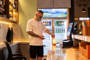 A person standing at a counter in a well-lit room with a refrigerator stocked with beverages and a television displaying a landscape. - Sunset Sorento Hotel & Apartment PhuQuoc (Phu Quoc)