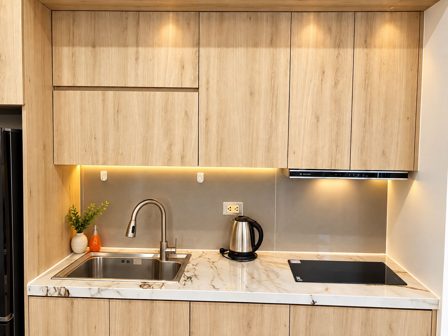 Een moderne keuken met houten kastjes, een roestvrijstalen spoelbak, een waterkoker en een zwarte inductiekookplaat.