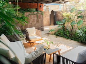 A patio area with a sofa, a chair, and a table, surrounded by greenery and a brick wall.