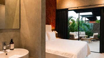 Habitación de hotel moderna con una cama grande, un baño con un lavamanos redondo y vistas a un jardín a través de una puerta corredera.