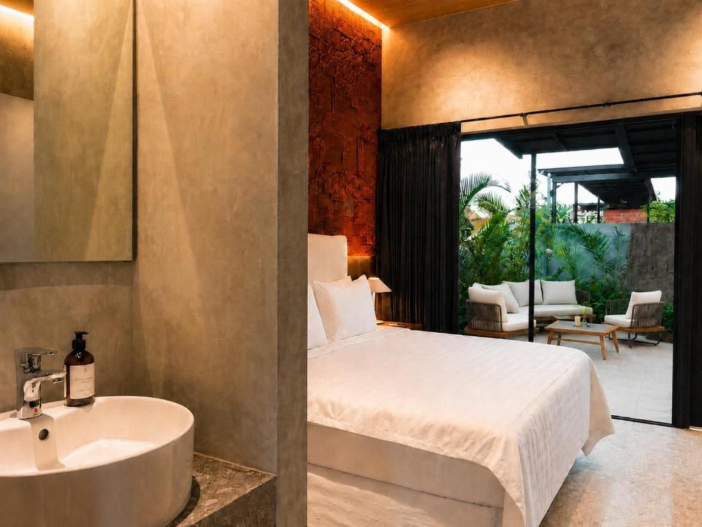 A modern hotel room with a large bed, a round sink, and a view of an outdoor patio with seating.