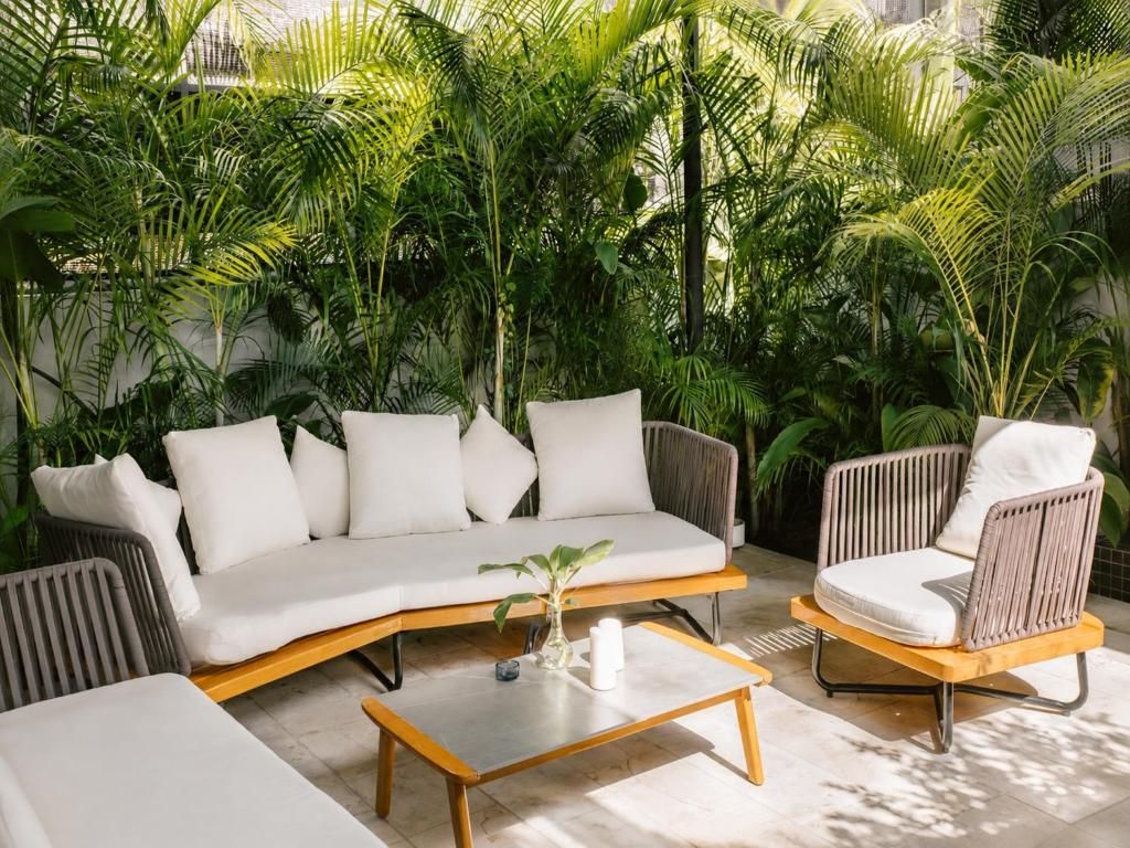 Un área de estar moderna al aire libre con un sofá y un sillón, rodeada de exuberante follaje tropical.