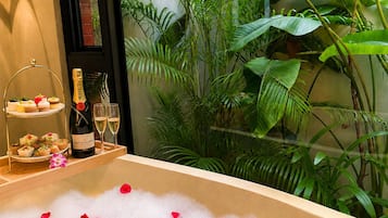 A bathtub filled with bubbles and rose petals, surrounded by lush green plants.