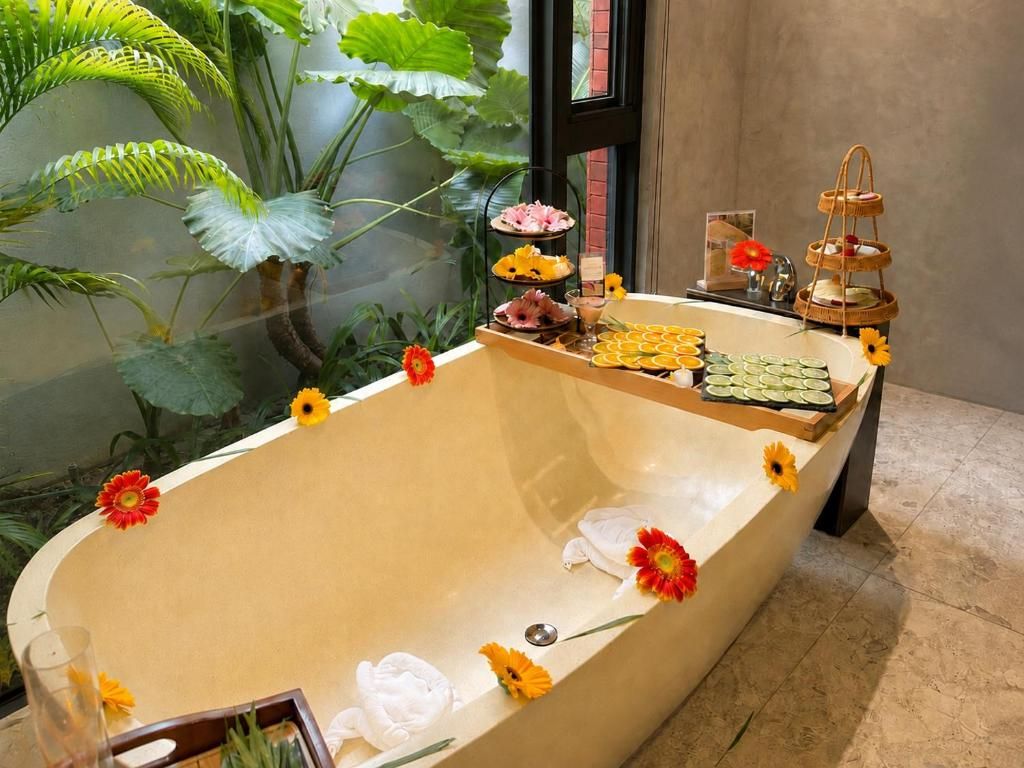 A bathtub with a tiered tray holding various items, surrounded by potted plants and flowers.