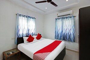 Ein Hotelzimmer mit einem Bett, roten Kissen, einer roten Decke, einem Deckenventilator und einer Klimaanlage.
