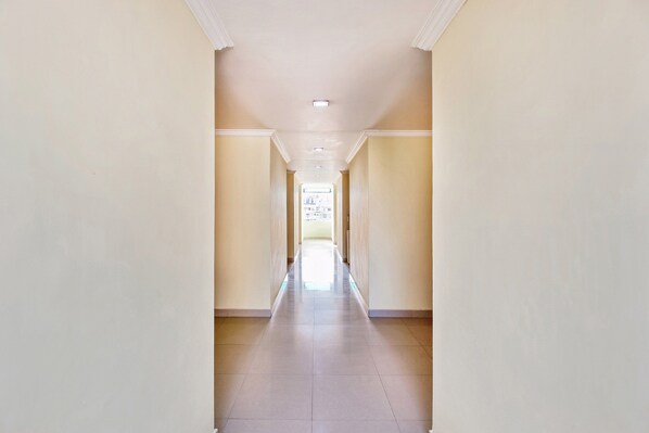 Um corredor comprido e estreito com piso de azulejos e paredes em tom creme.