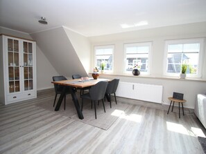 A dining area with a table and chairs, a cabinet with glass doors, and a radiator. - Holiday Apartment With 2 Bedrooms (Sylt)
