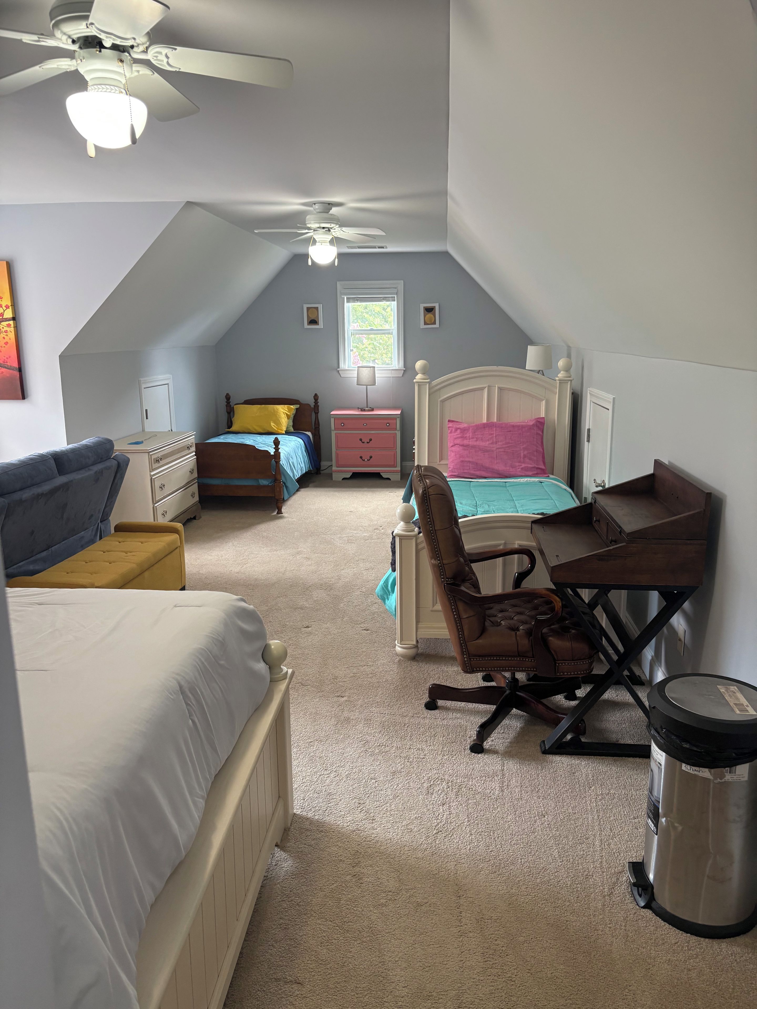 A bedroom with two beds, a desk, a chair, a ceiling fan, and a window.