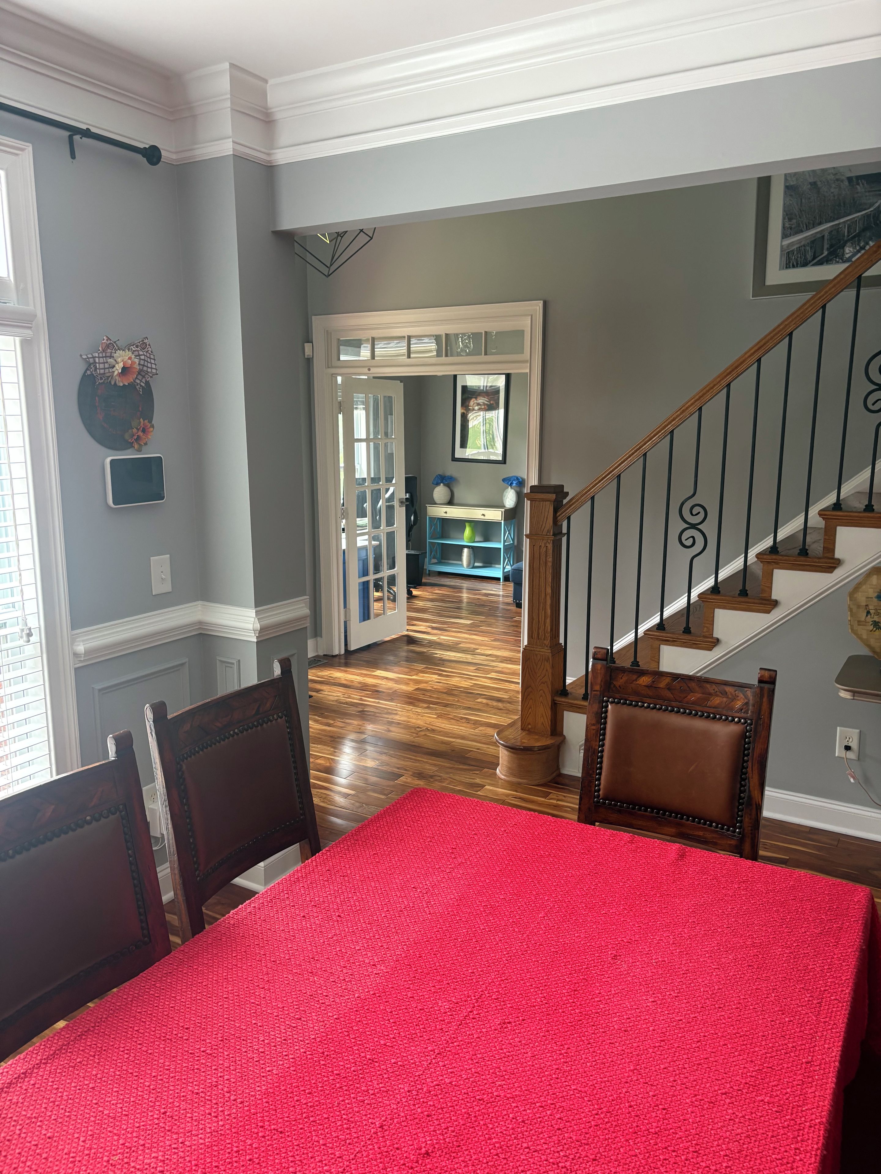 A dining area with a red tablecloth, wooden chairs, a staircase with a railing, and a hallway leading to another room.