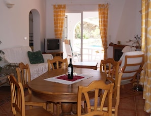A dining area with a round wooden table, chairs, a television, and a view of an outdoor pool. - Holiday Home in Torrox With Swimming Pool (Torrox)