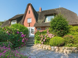 A traditional thatched-roof house with a stone staircase leading to the entrance, surrounded by lush greenery and flowering plants. - Holiday Apartment in Kampen With Wi-fi (Kampen)