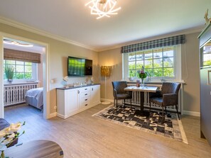 A modern kitchen with a dining area, a television mounted above the counter, and a window with a view of greenery. - Holiday Apartment in Kampen With Wi-fi (Kampen)