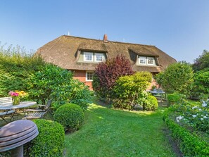 A thatched-roof house with a well-maintained garden and a dining area with outdoor furniture. - Holiday Apartment in Kampen With Wi-fi (Kampen)
