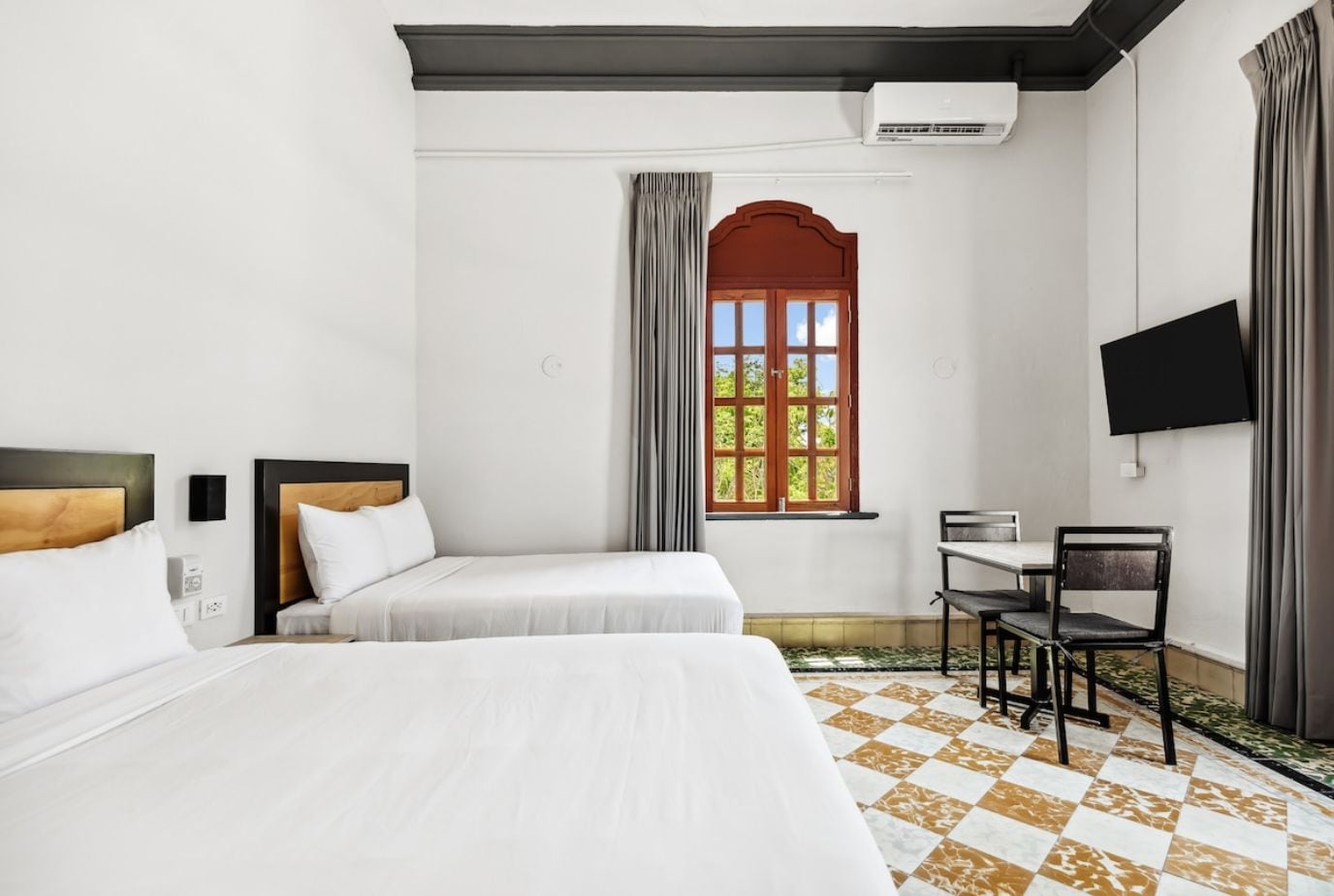 A hotel room with two beds, a desk, a chair, a TV, and a window with curtains.