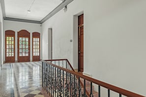 Un pasillo con piso de cuadros, puertas de madera con paneles de vidrio y una escalera con barandilla de metal.