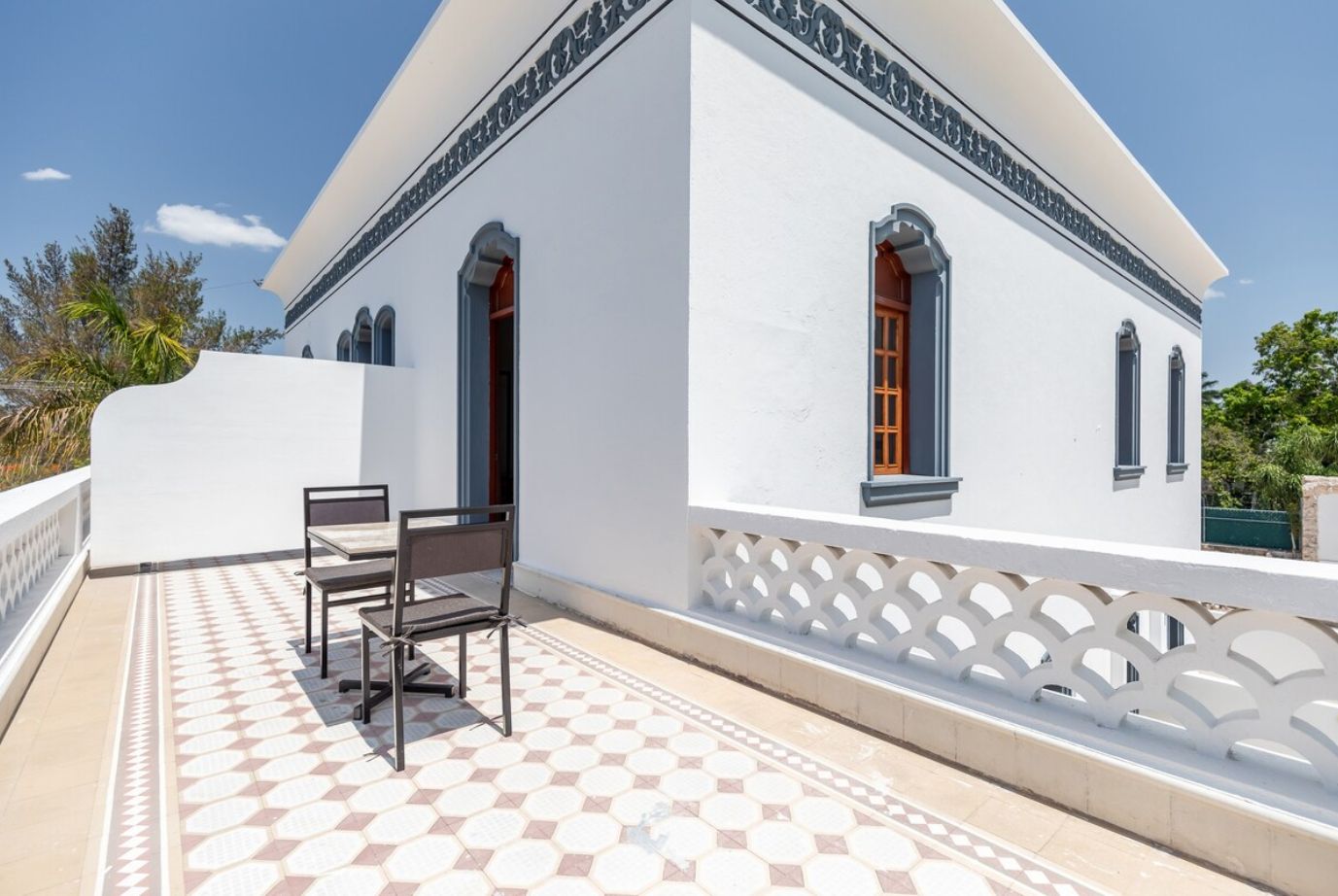 A white building with a tiled patio, a white fence, and a bench.