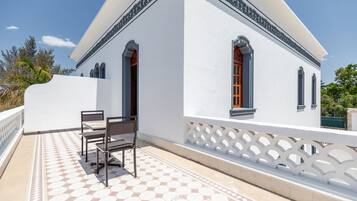 A white building with a tiled patio, a white fence, and a bench.