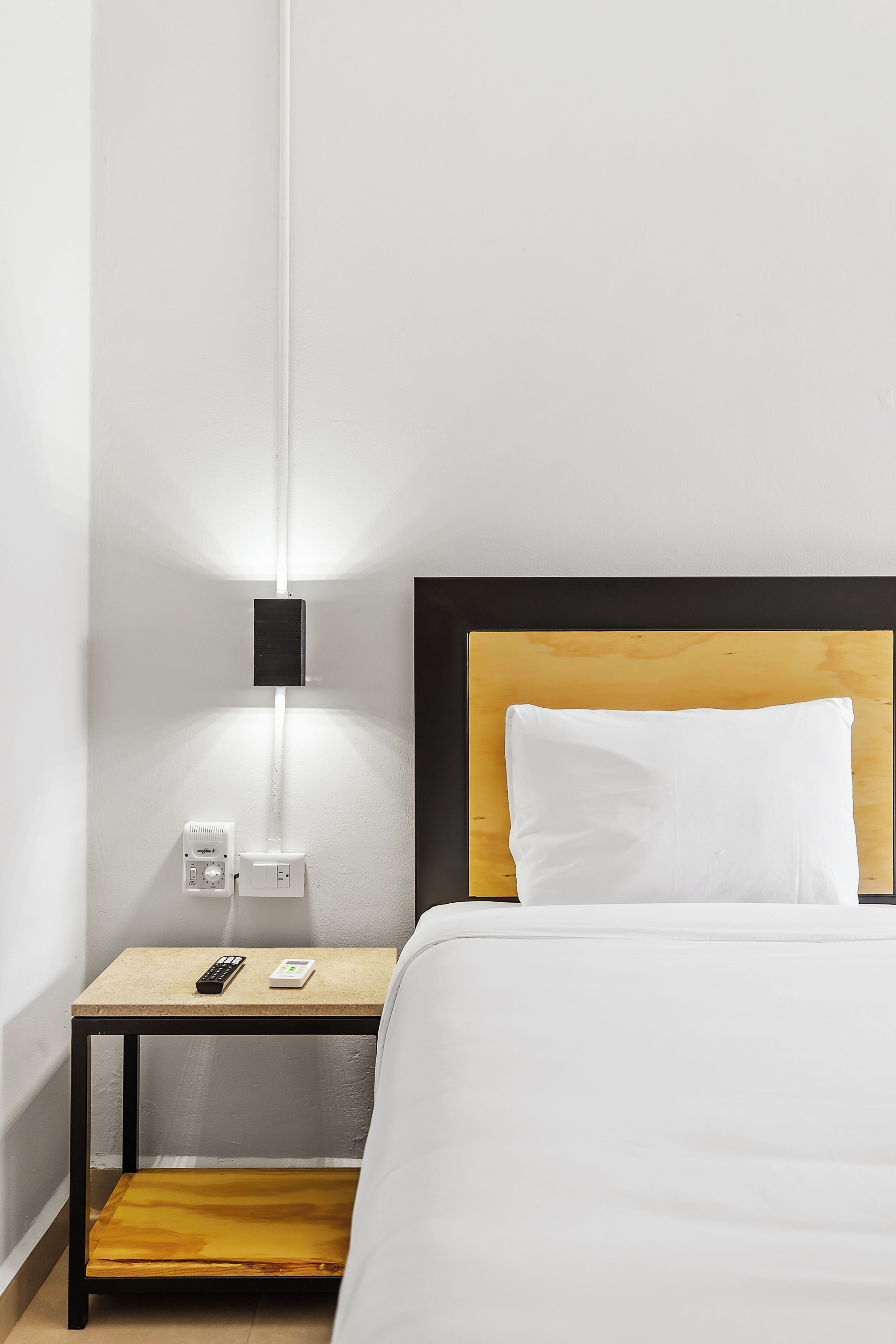 Ein Hotelzimmer mit Bett, Nachttisch, Fernbedienung und Steckdose.